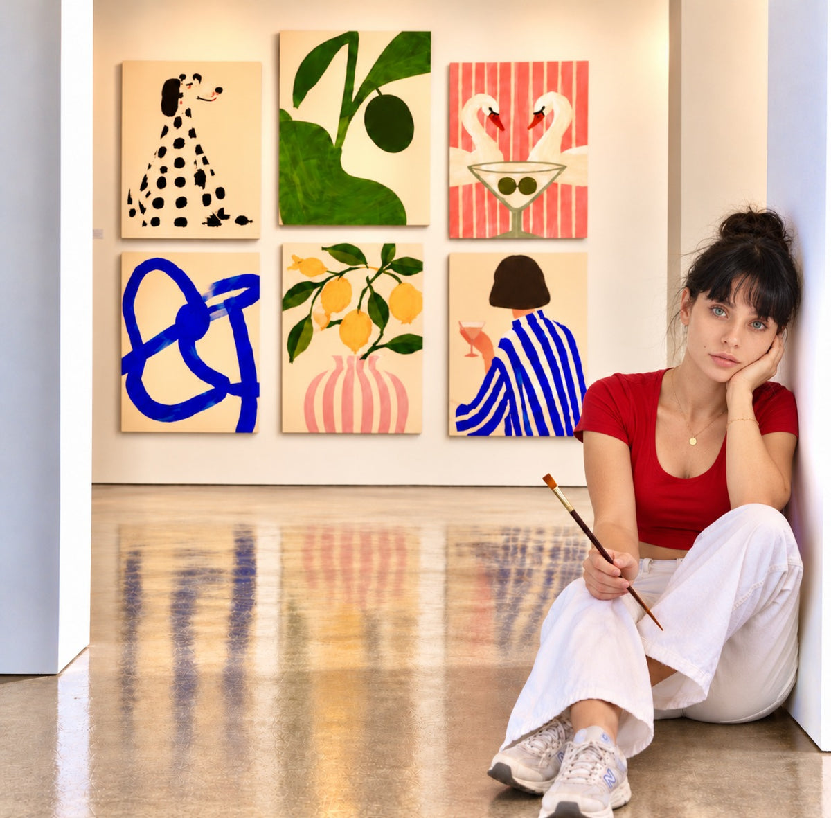 An artist sitting on the floor of a white gallery in front of six framed prints